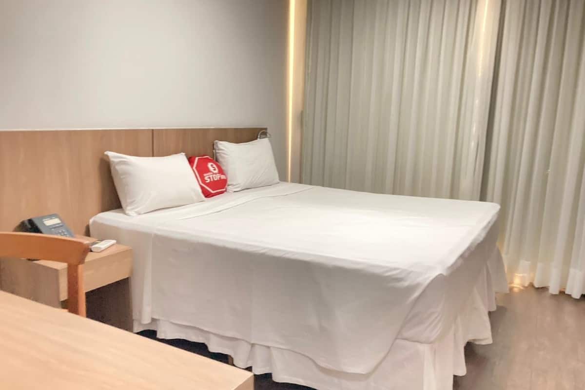 Siisti hotellihuone, jossa on huolitellusti pedattu sänky, puinen yöpöytä, jossa on puhelin, ja punainen, liikennemerkkiä muistuttava koristetyyny.