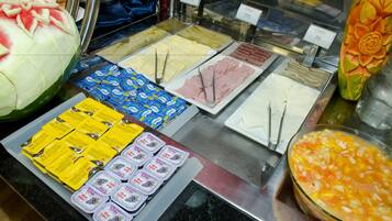 A buffet with various food items including a watermelon, cheese, ham, and a bowl of fruit salad.