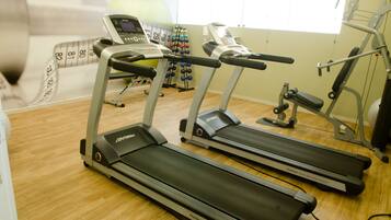 Un gimnasio con dos cintas de correr, un banco para pesas y una báscula digital.