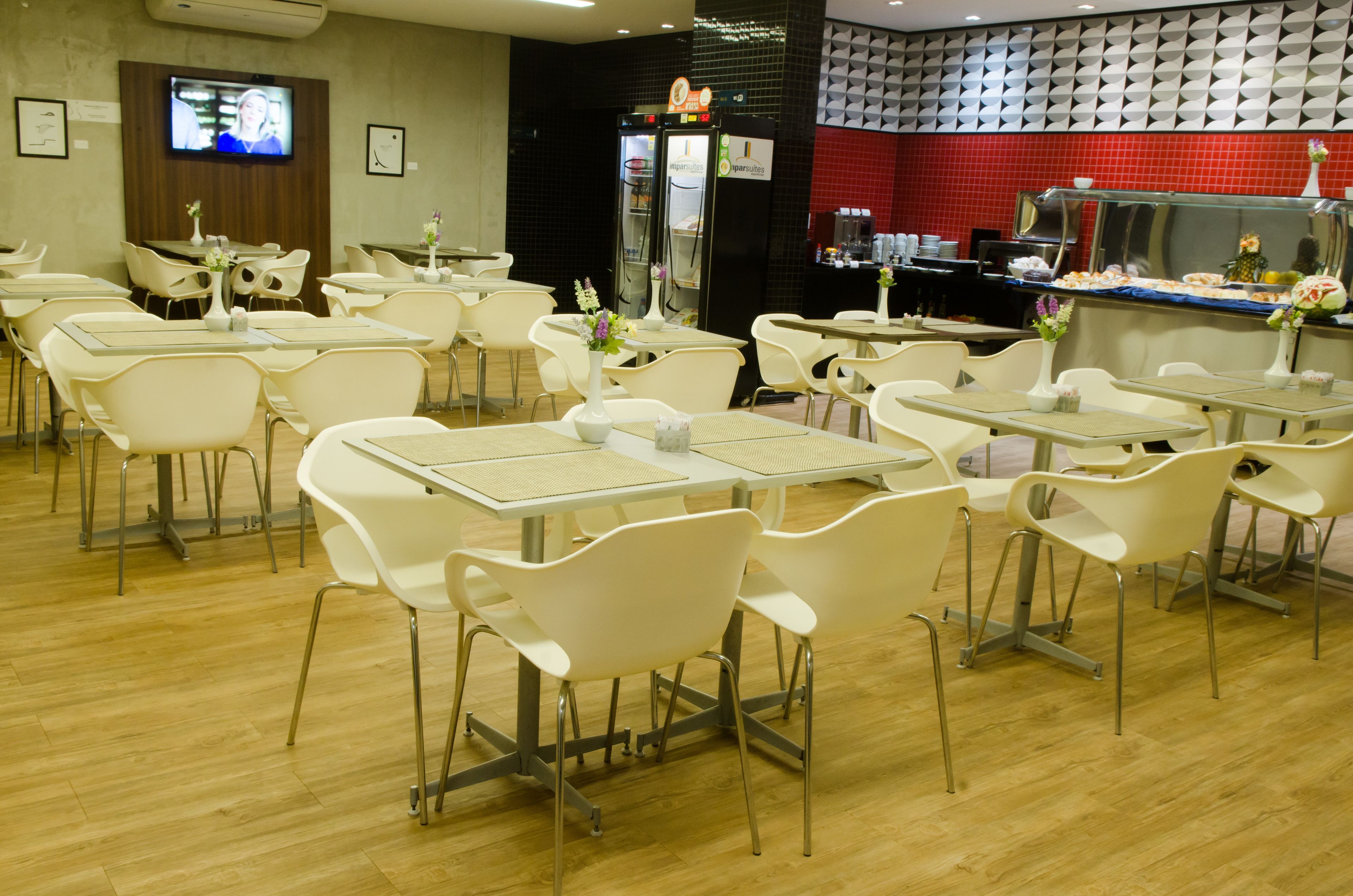 Un restaurante con sillas y mesas blancas, un televisor en la pared y un mostrador de buffet con comida.