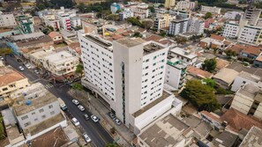 A multi-story hotel with a modern design, featuring a central courtyard and a mix of residential and commercial buildings in the surrounding area. - Ímpar Suítes Expominas (Belo Horizonte)