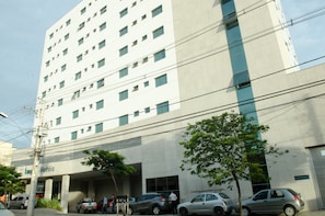 A multi-story hotel with a modern facade, several parked cars, and a few pedestrians. - Ímpar Suítes Expominas (Belo Horizonte)