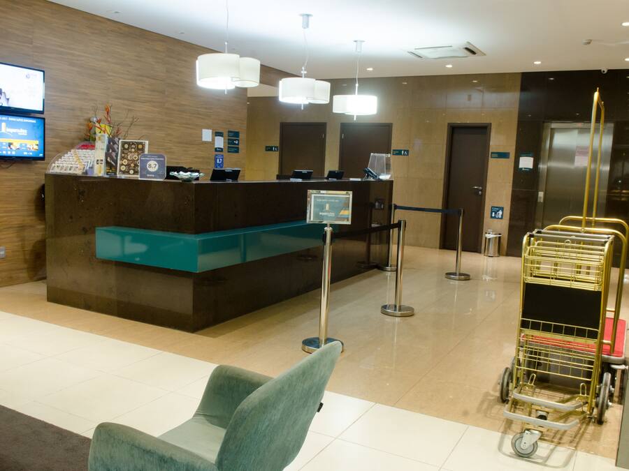 Zona de recepción de un hotel con mostrador de recepción, televisor y quiosco de autoservicio.