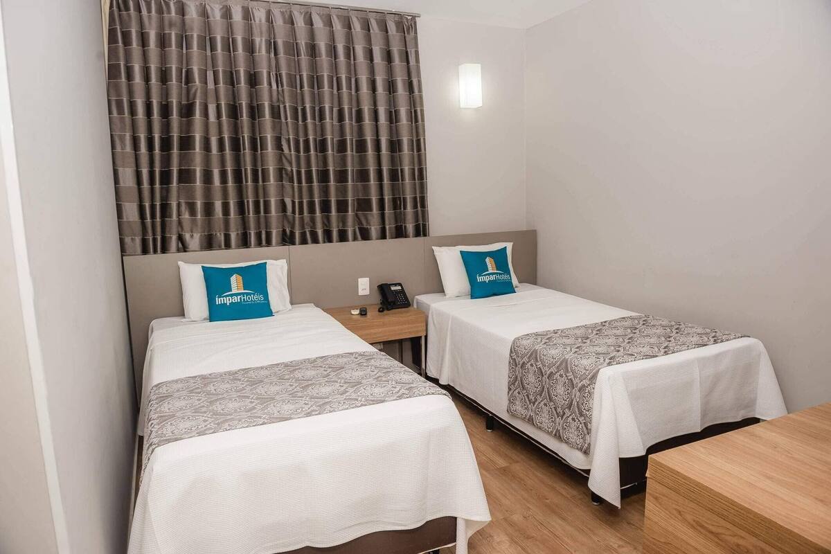A hotel room with two single beds, a wooden nightstand, a telephone, and a window with curtains.
