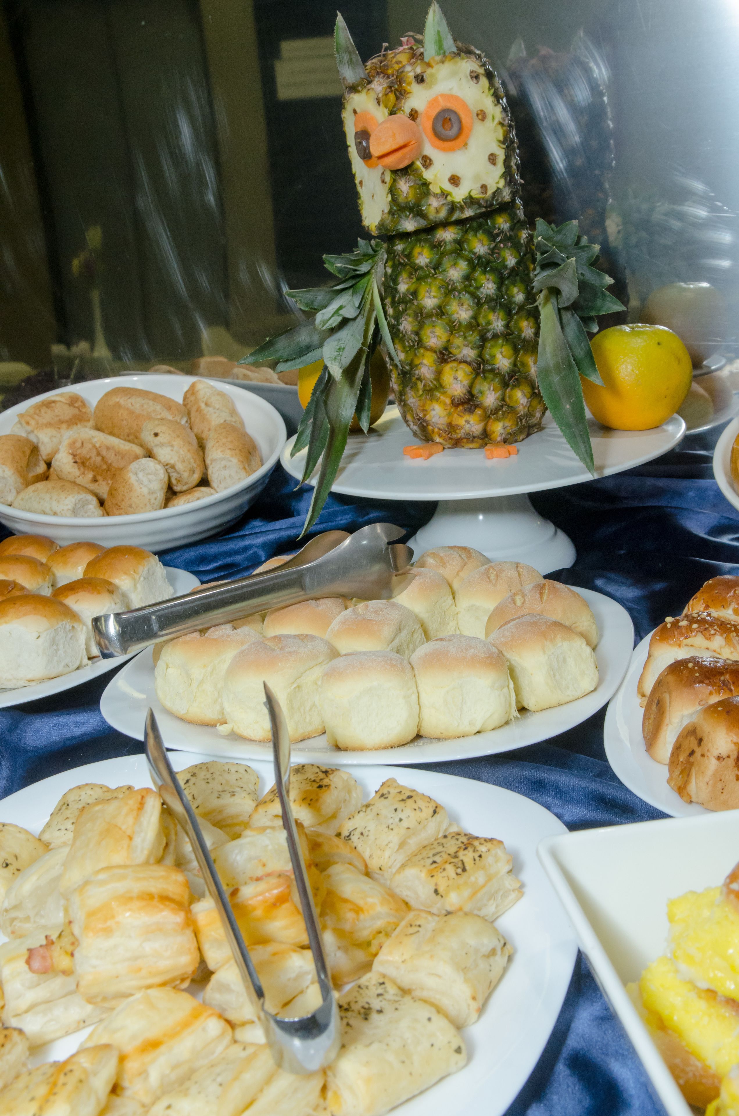 Une table de buffet proposant divers plats, notamment des petits pains, des pâtisseries et un ananas décoré de manière originale.