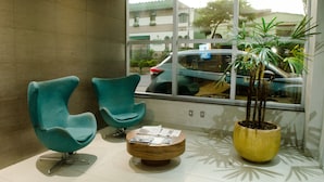 A lobby with two teal chairs, a wooden coffee table with magazines, and a large potted plant. - Ímpar Suítes Expominas (Belo Horizonte)