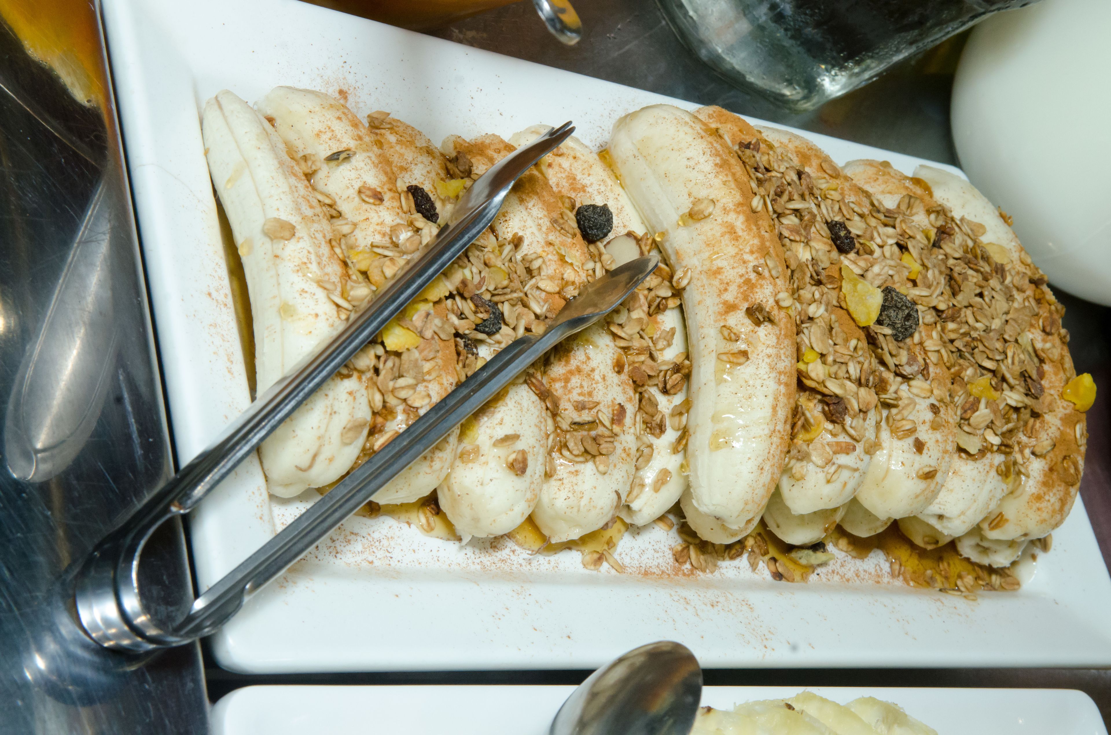 A white plate with sliced bananas topped with granola and raisins.