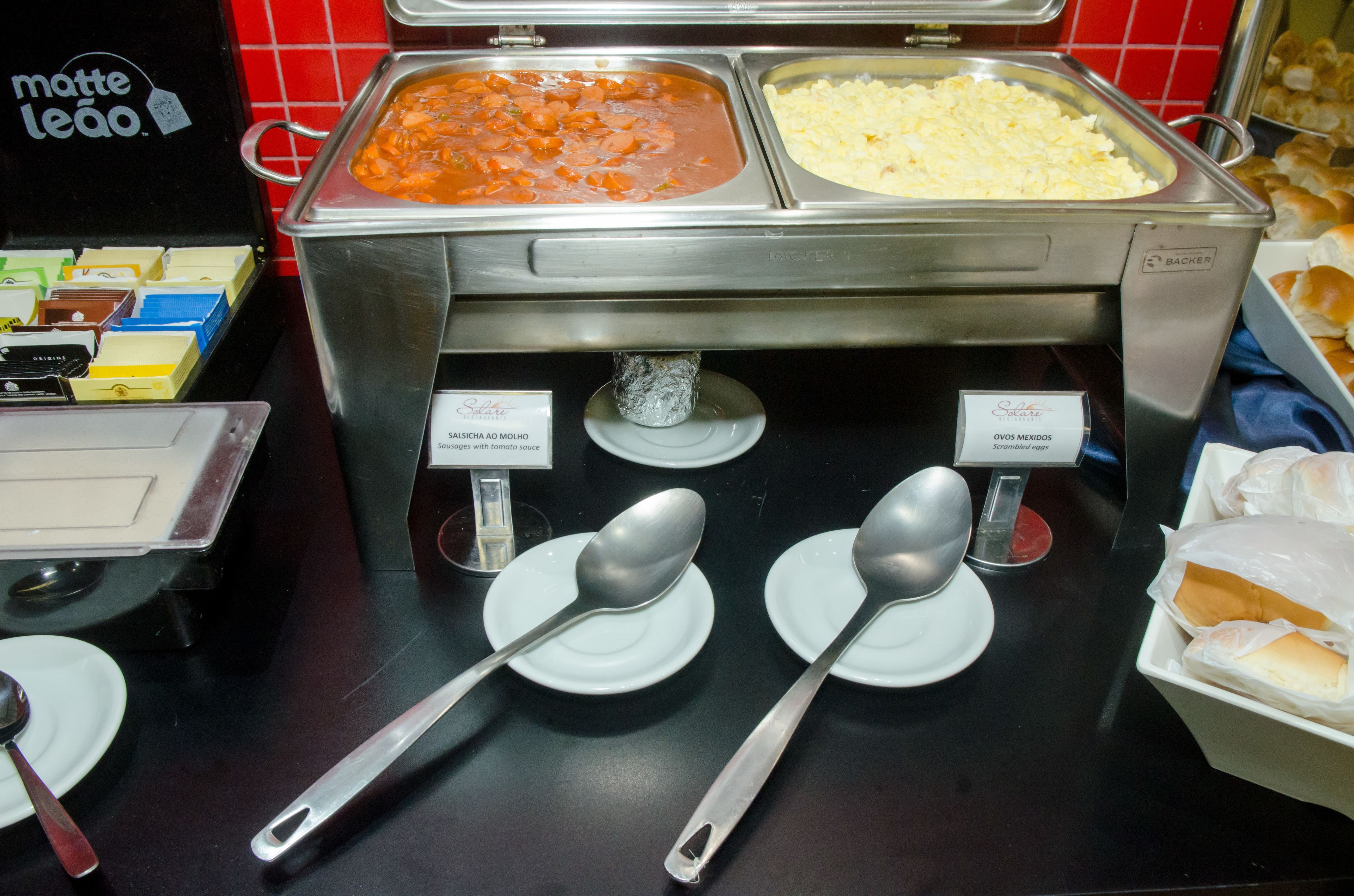 Un bufé con diversas opciones de comida, incluyendo un plato a base de tomate y un plato de arroz, con utensilios de servir y platos en la barra.
