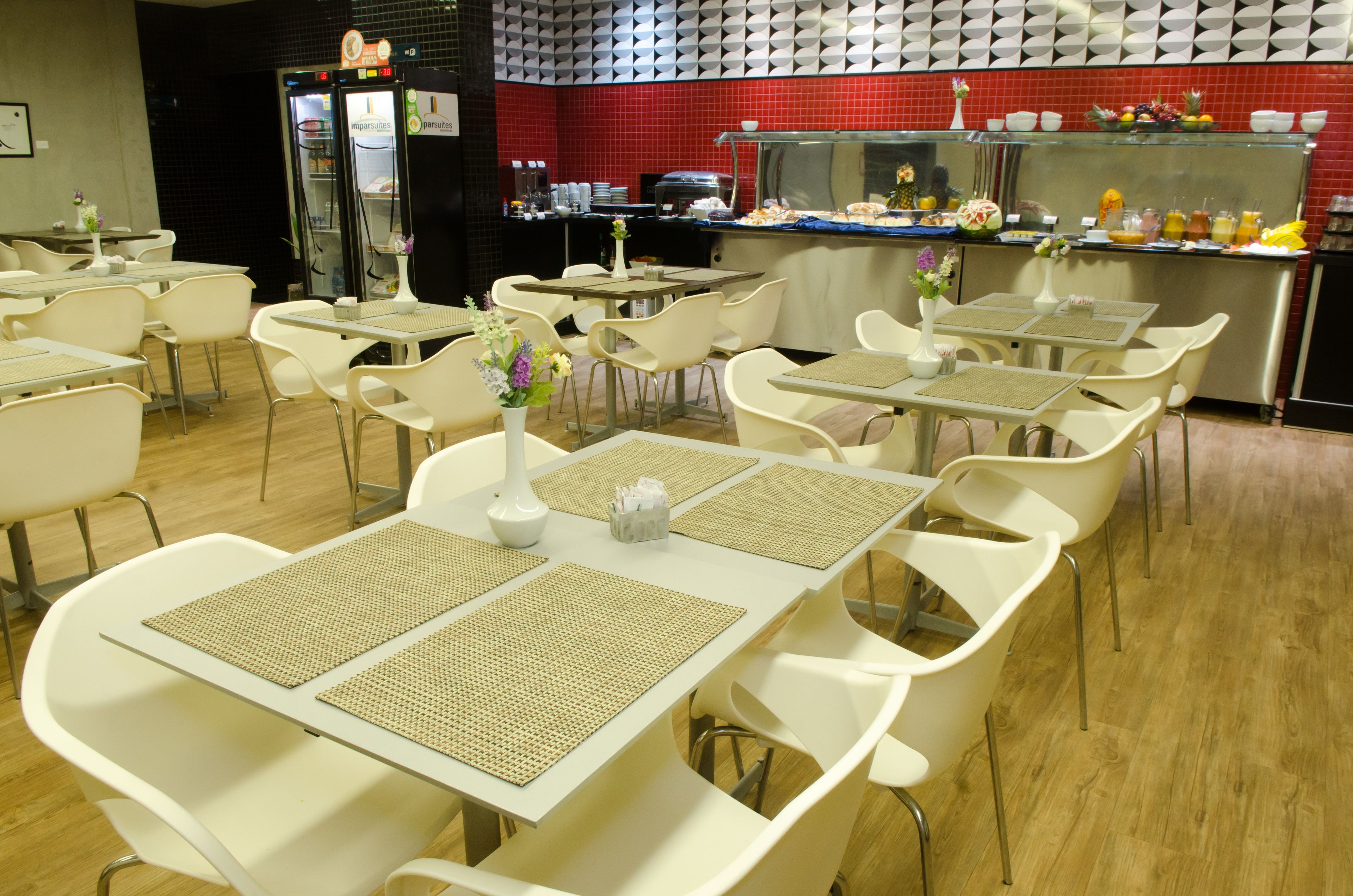 Eine Cafeteria mit weißen Tischen und Stühlen, einem Kühlschrank und einer Theke mit Speisen.