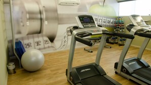 A gym with treadmills, a stationary bike, and a wall with a large apple and dumbbells. - Ímpar Suítes Expominas (Belo Horizonte)