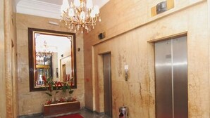 A lobby with a red carpet, a chandelier, a large mirror, and two elevators. - City Hotel Porto Alegre (Porto Alegre)