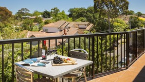 Un balcon avec une table dressée pour un repas, agrémenté d’une bouteille, de verres et d’un plateau de fruits.