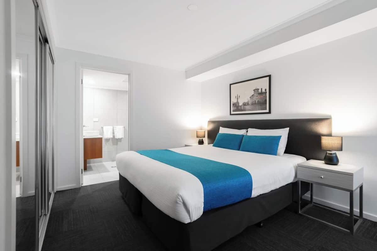 Ein modernes Hotelzimmer mit einem großen Bett, Nachttischen, einem Beistelltisch und einem gerahmten Bild an der Wand.