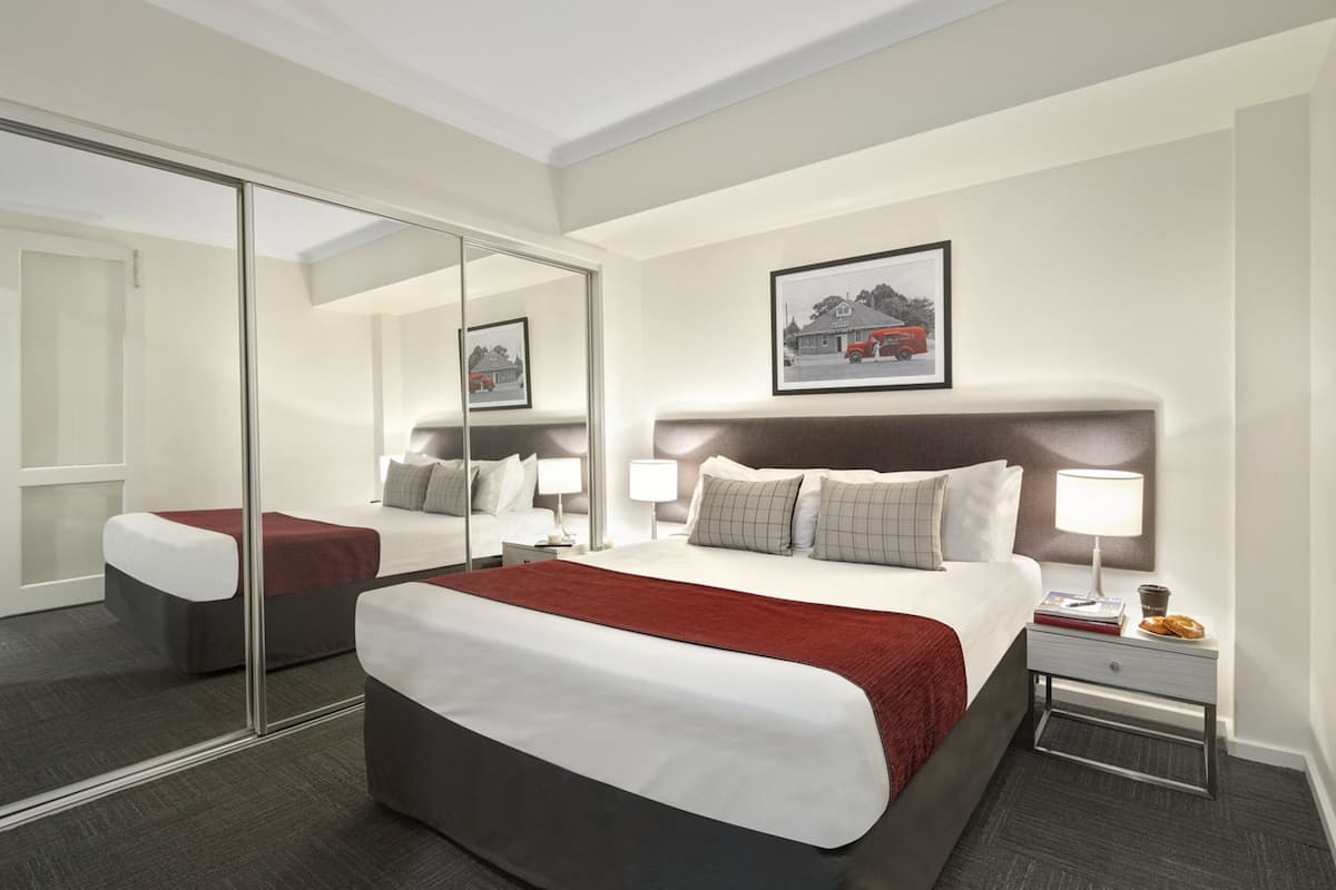 Ein modernes Hotelzimmer mit einem großen Bett, einem Nachttisch mit Lampe, einem Spiegel und einem gerahmten Bild an der Wand.