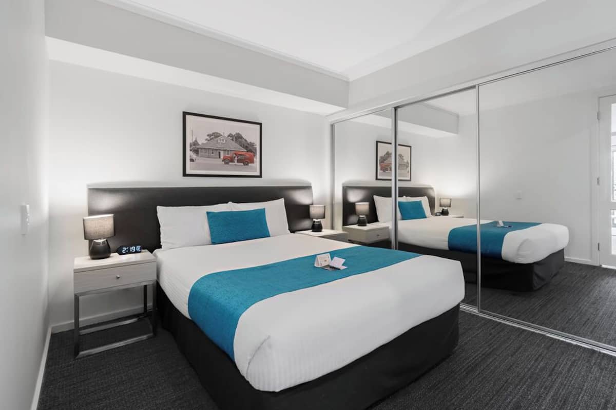 A hotel room with a large bed, a bedside table with a lamp, a nightstand, and a mirror.
