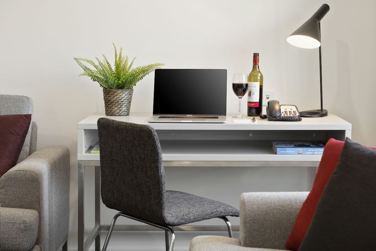 Ein moderner Arbeitsplatz mit Laptop, einer Weinflasche, einem Telefon und einer Schreibtischlampe.
