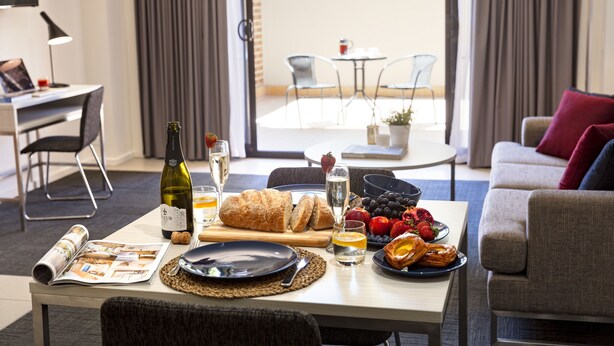 Un coin repas avec une table mise pour le petit-déjeuner, comprenant du pain, des fruits et une bouteille de vin.