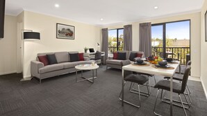 Un salon moderne comprenant un canapé, une table basse, une table à manger et des chaises. On y trouve une fenêtre avec des rideaux, un tableau accroché au mur et un balcon avec vue.