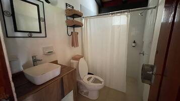 A bathroom with a sink, mirror, towel rack, toilet, and shower curtain.