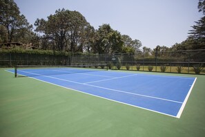 Un court de tennis avec un filet, entouré d’une clôture et d’arbres.