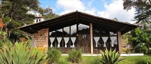 Un pavillon rustique, doté d’une base en pierre et d’un toit en bois, entouré d’une végétation luxuriante.