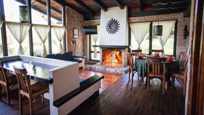 A cozy room with a stone fireplace, wooden furniture, and large windows with curtains.