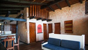A rustic interior with a stone wall, wooden ceiling beams, a blue sofa, and a wooden dining table with chairs.