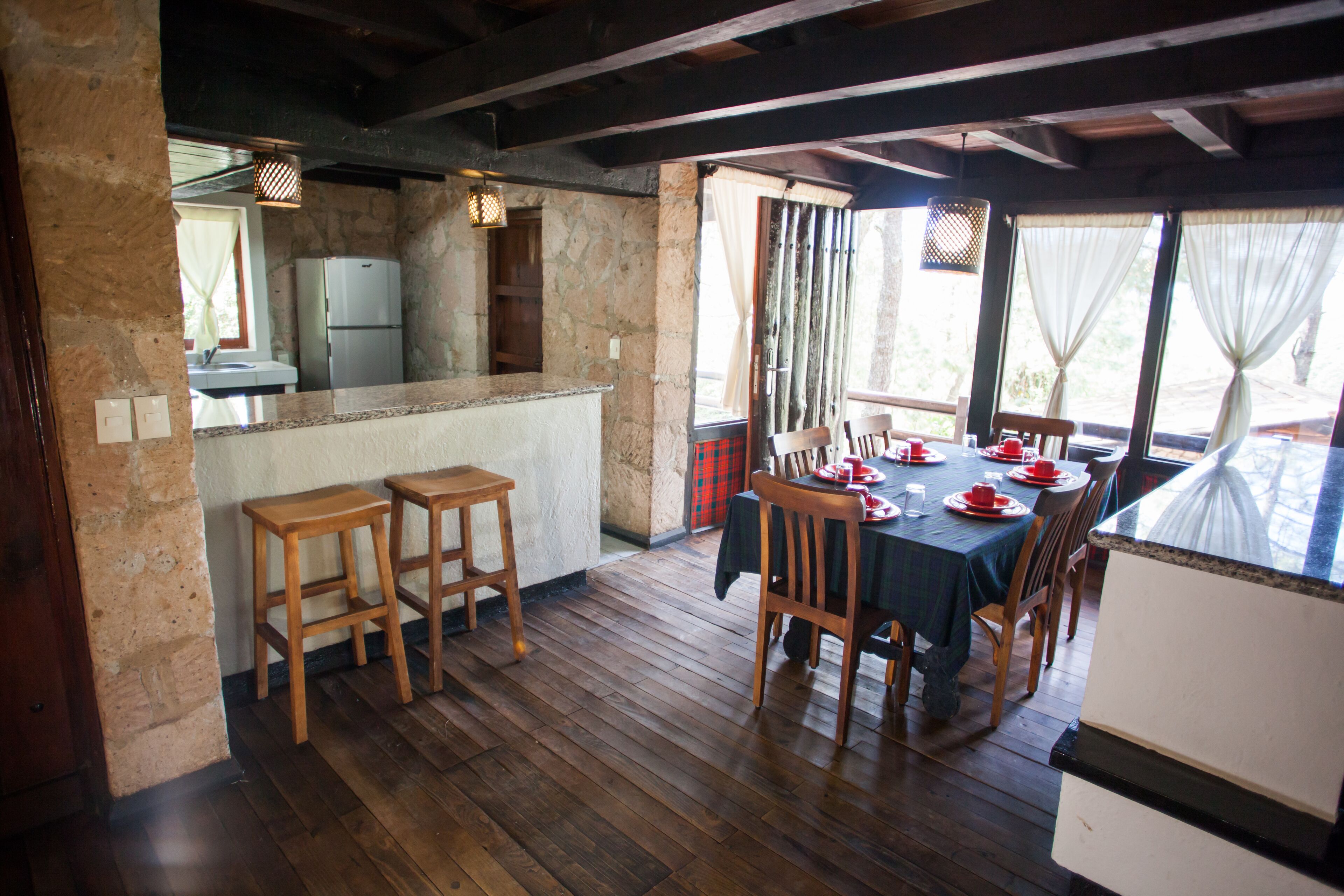 A rustic kitchen with a stone wall, wooden stools, and a dining area with a table set for four.