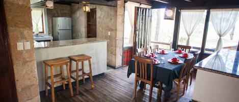 Une cuisine rustique avec un mur en pierre, des tabourets en bois et un coin repas avec une table dressée pour quatre personnes.