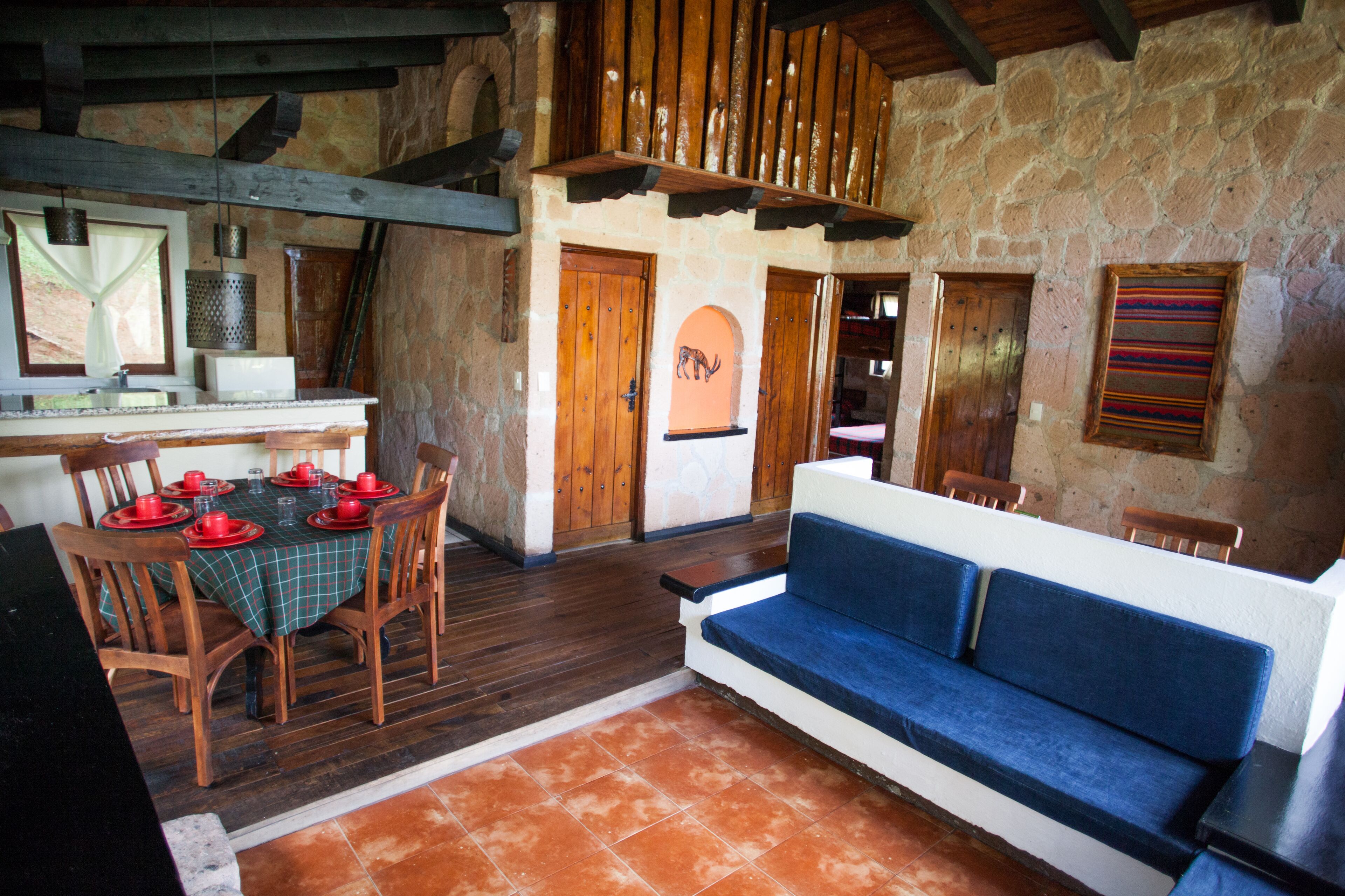 Un comedor rústico con una mesa de madera dispuesta para cuatro, un sofá azul y paredes de piedra.