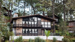 A traditional wooden house with a stone facade, surrounded by lush greenery and trees.