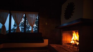 A fireplace with a fire, a window with curtains, and a stone bench.