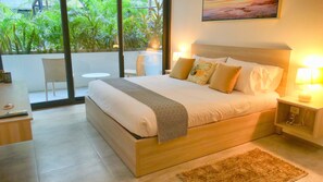 A modern bedroom with a large bed, bedside lamps, a small table, and a view of greenery outside.