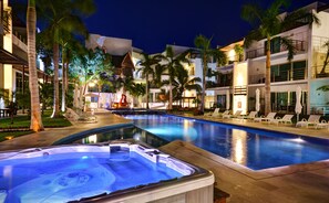 A swimming pool area with lounge chairs and a hot tub, surrounded by palm trees and modern buildings. - Luxury Condo Boutique (Playa del Carmen)