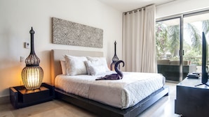 Ein modernes Schlafzimmer mit einem großen Bett, einer Zierlampe, einem Wandbild und Blick ins Freie durch eine Schiebetür.