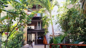 Ein Hotel mit Eingangsbereich, einer Rezeption und einer Treppe, die zu den oberen Stockwerken führt, umgeben von üppigem Grün.