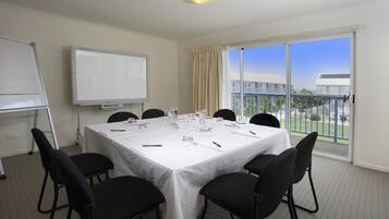 A conference room with a white table, black chairs, a whiteboard, and a view of a building through large windows.