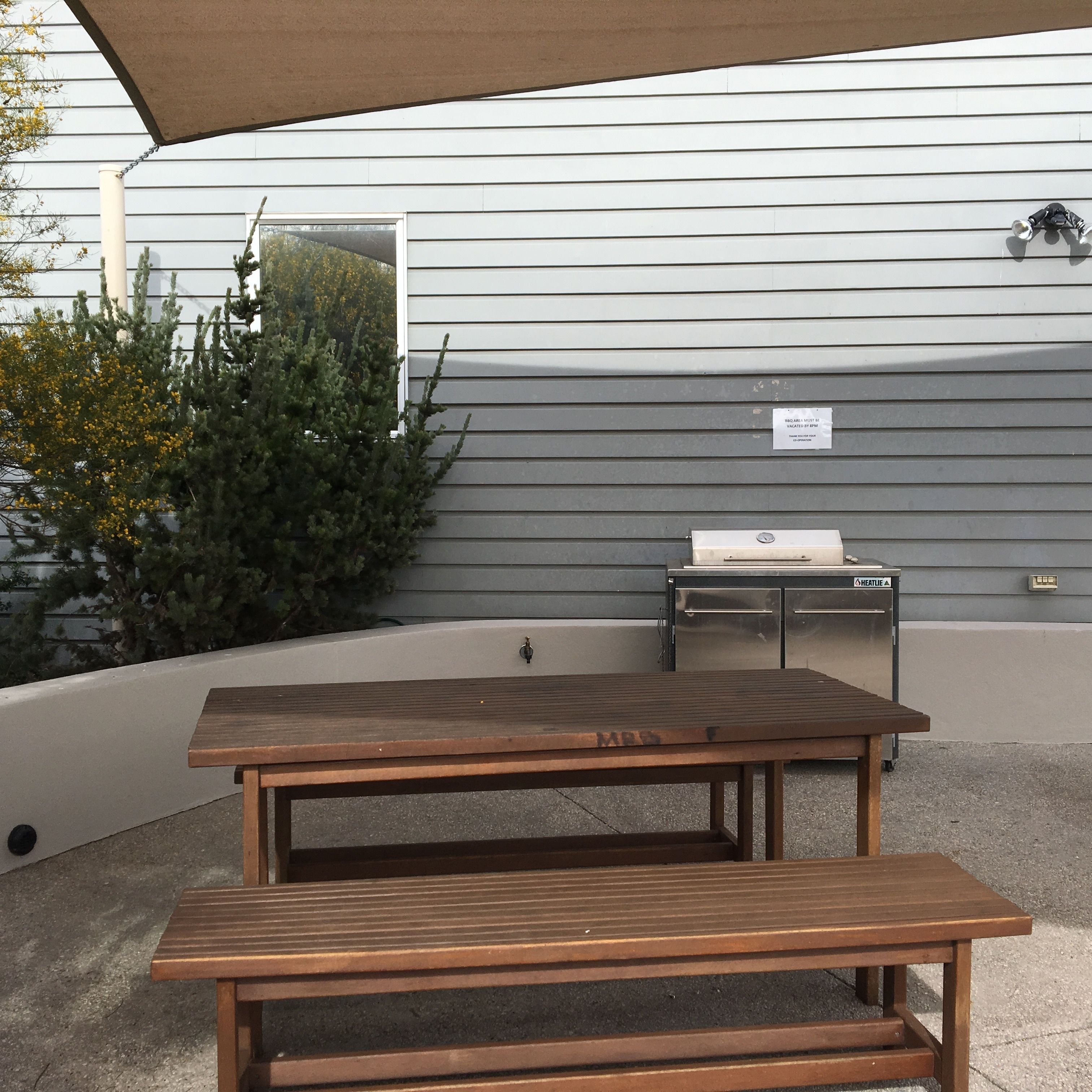 An outdoor patio area with a wooden table and bench, a grill, and a water feature.
