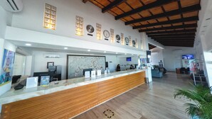 A reception area with a wooden reception desk, multiple clocks on the wall, and a large abstract painting above the desk. - Hotel Splash Inn Nuevo Vallarta (Nuevo Nayarit)