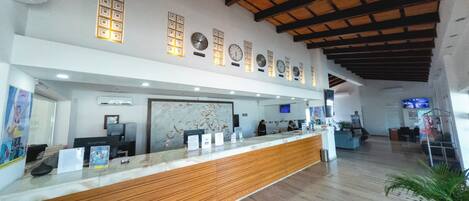 A reception area with a wooden reception desk, multiple clocks on the wall, and a large abstract painting above the desk.