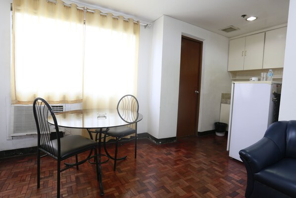A compact kitchen with a refrigerator, a dining table with chairs, and a window with curtains.