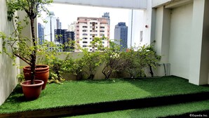 A balcony with artificial grass, potted plants, and a view of city buildings. - The Victor Hotel (Makati)