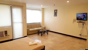 A hotel room with a bed, a sofa, a small table, a TV, and a window. - The Victor Hotel (Makati)