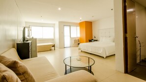 A modern hotel room with a bed, a sofa, a glass coffee table, and a desk with a computer. - The Victor Hotel (Makati)