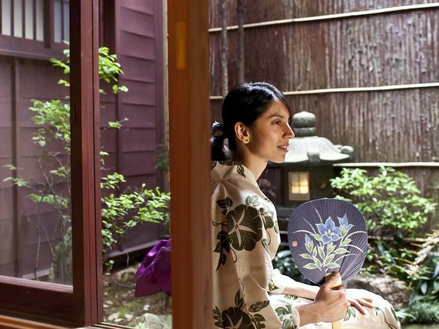 A traditional Japanese room with tatami flooring, a shoji screen door, and a view of a garden with a wooden fence and greenery.