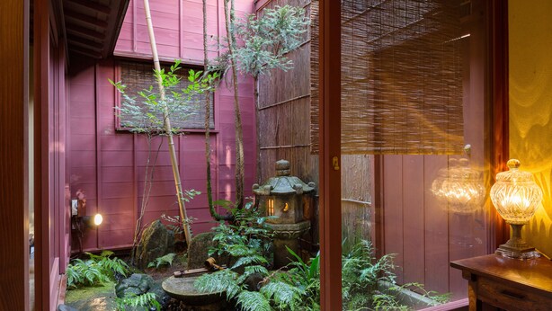 Un jardín japonés tradicional con un farol de madera, un pequeño estanque y abundante vegetación.