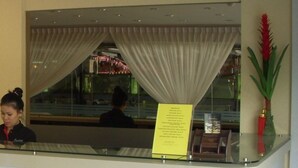 A reception desk with a glass partition, a reception area, and a window with curtains. - Stay Inn Hotel (Kota Kinabalu)