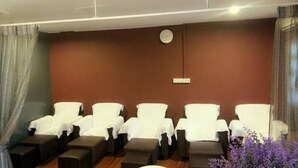 A room with five white massage chairs arranged in a row, a wooden floor, and a brown wall with a clock. - Stay Inn Hotel (Kota Kinabalu)