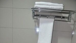 A bathroom with a white toilet, a shower, and a towel rack with two towels. - Stay Inn Hotel (Kota Kinabalu)
