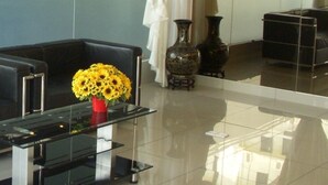 A black leather sofa, a glass coffee table with a red vase of yellow flowers, and a black vase on a reflective floor. - Stay Inn Hotel (Kota Kinabalu)